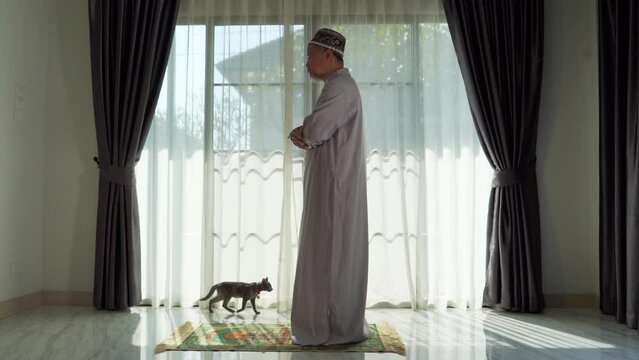 An elderly Muslim man with a gray beard prays at home during the coronavirus pandemic. Covid-19, quarantine concept	