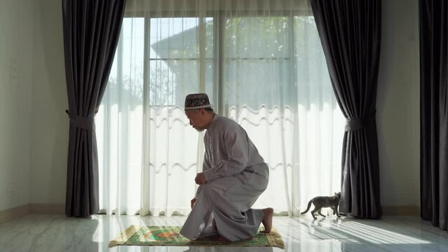An elderly Muslim man with a gray beard prays at home during the coronavirus pandemic. Covid-19, quarantine concept	