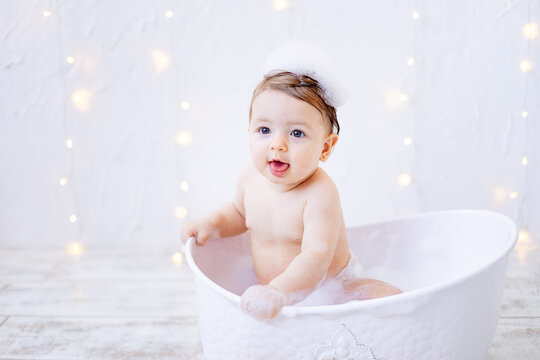 a joyful baby girl of six months is bathing in a bubble bath, a small child is having fun playing with water, the concept of care and hygiene