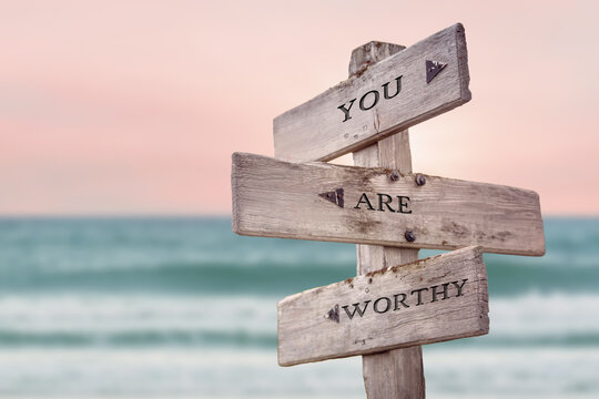 you are worthy text quote written on wooden signpost by the sea. Positive pink turqoise pastel theme.