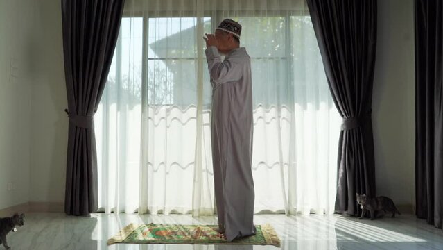 An elderly Muslim man with a gray beard prays at home during the coronavirus pandemic. Covid-19, quarantine concept	