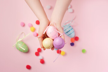 Children's hands hold Easter shiny eggs. Decorative eggs and fluffy balls on a pink background. Background for your project for the holiday happy easter