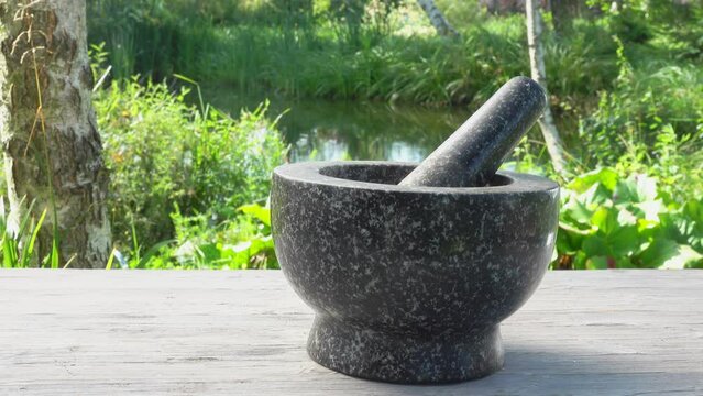 Hand is putting fresh spices into the grey stone mortar in slow motion outdoors