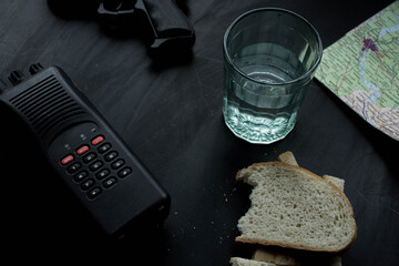 Walkie-talkie, a glass, a piece of bread and a map on a black background
