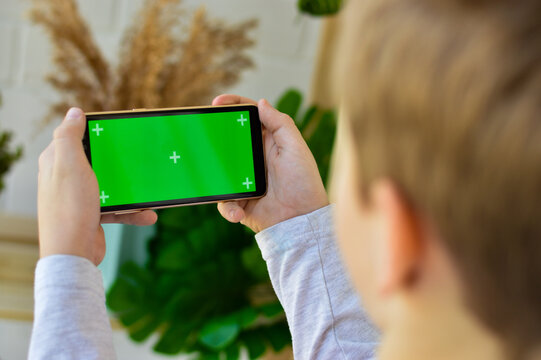 The child is holding a phone in his hand with a green screen.