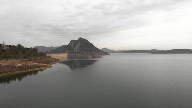 Aerial images showing a huge reservoir from 120 meters high.  In the background a large mountain with a medieval castle on it.  Camera approaching to the dam.