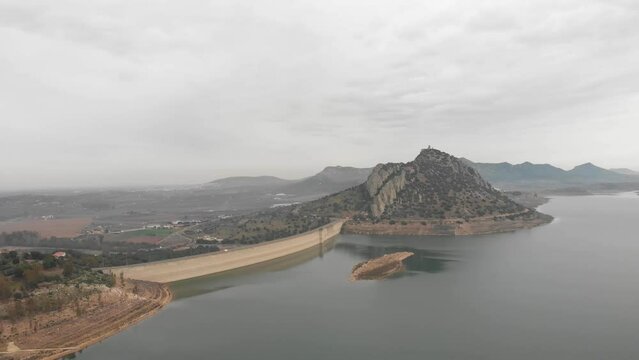 Aerial images showing a huge reservoir from 120 meters high.  In the background a large mountain with a medieval castle on it.  Camera turns to the right focusing the island in the foreground.
