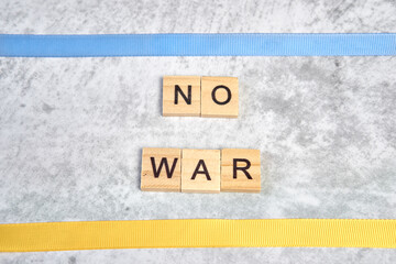 phrase no war is laid out of wooden squares on a gray background with flag of ukraine with blue and yellow ribbon. Concept of peace, war in Ukraine