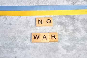 phrase no war is laid out of wooden squares on a gray background with flag of ukraine with blue and yellow ribbon. Concept of peace, war in Ukraine