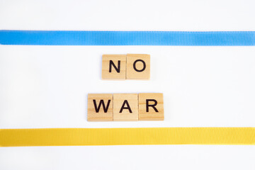 phrase no war is laid out of wooden squares isolated on white background. with flag of ukraine with blue and yellow ribbon. Concept of peace, war in Ukraine