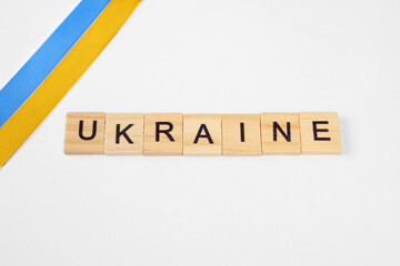 phrase ukraine is laid out of wooden squares isolated on white background. with flag of ukraine with blue and yellow ribbon. Concept of peace, war in Ukraine