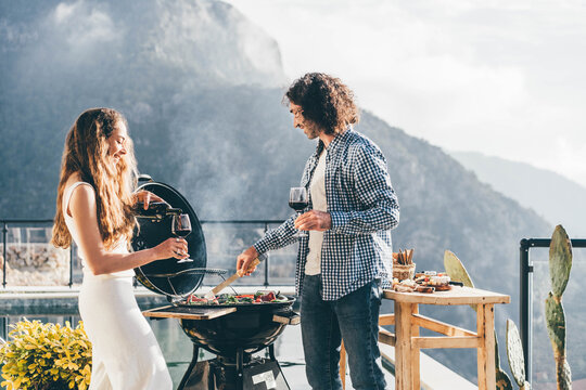 Happy couple making barbecue on a terrace with beautiful view.