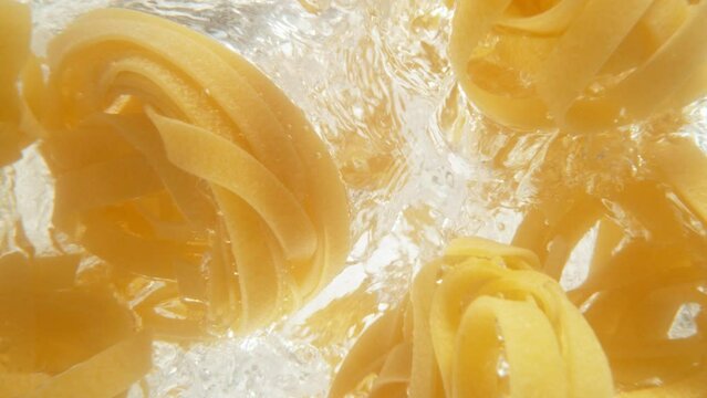 Super slow motion of falling uncooked italian pasta Tagliatelle into water, white background. Filmed on high speed cinema camera, 1000 fps.