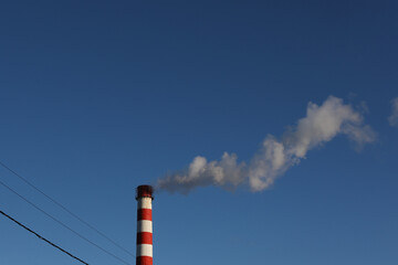 Red and white industrial chimney with smoke against blue sky background
