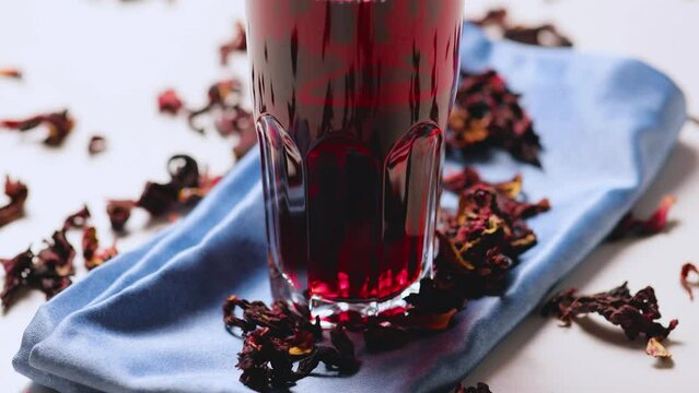 Hibiscus tea in a glass. Hibiscus leaves for making trendy tea. Red hibiscus tea on a blue napkin. Healthy food concept