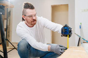 carpenter in protective gloves and glasses makes measurements on wood