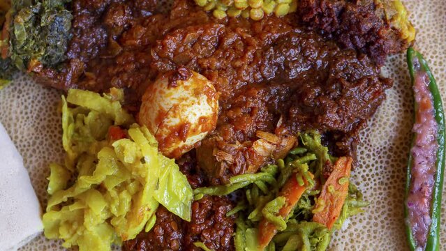 Zoom in on Injera served with chicken, egg, doro wat, berbere, vegetables and lentils. Injera, a traditional staple food of Ethiopia, is a sourdough flatbread made from teff flour.