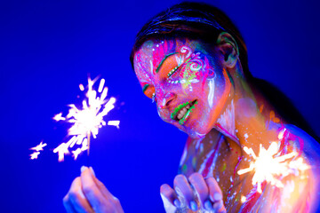 Woman with sparkler in neon light. Beautiful model girl colorful bright fluorescent makeup. Holiday...