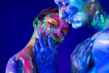 Portrait of a beefy man and woman painted in ultraviolet powder. Body art glowing in ultraviolet light