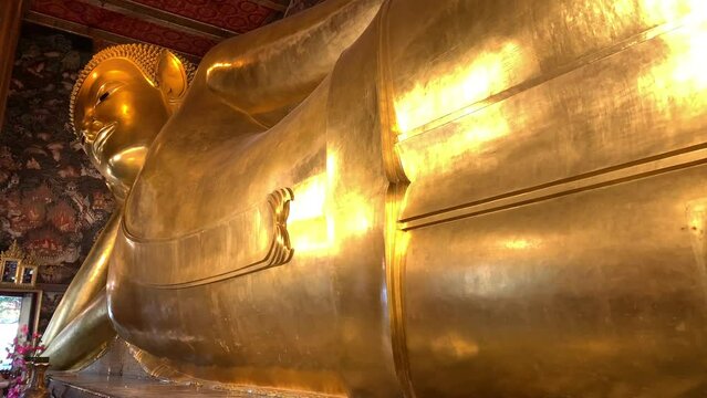 BANGKOK, THAILAND - Circa November, 2021: Golden Reclining Buddha Statue at Wat Pho, world heritage buddhist temple. This sleeping posture known as sihasaiyas. Beautiful background wall - Low angle 