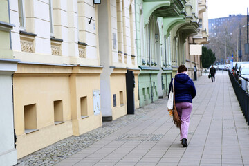 Kobieta ze słuchawkami na głowie idzie chodnikiem we Wrocławiu. - obrazy, fototapety, plakaty
