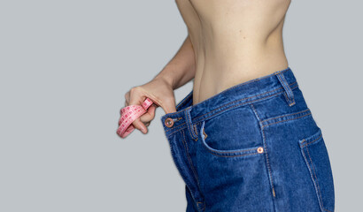 young woman with measure tape on hand is showing loose jeans, Loss Weight. diet and health concept. Slim beautiful woman's abs, girl wears jeans large size. mother's belly after giving birth.