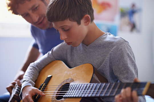 Studying the strings. Shot of a boy learning to play guitar from his father.