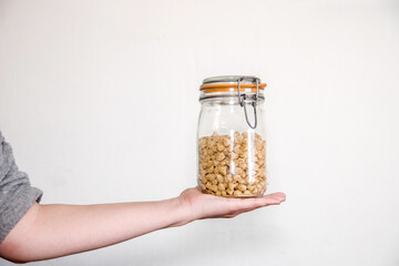 Una mano sujetando un tarro de cristal lleno con granos de soja texturizada. Concepto de alternativas veganas a la carne. Proteína vegetal. - obrazy, fototapety, plakaty
