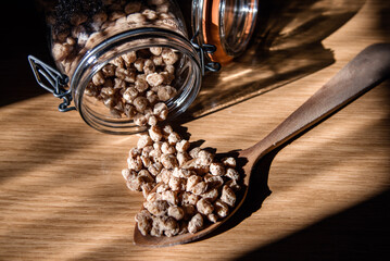 Cucharón de madera lleno de granos de soja texturizada gruesa junto a un tarro de cristal volcado...