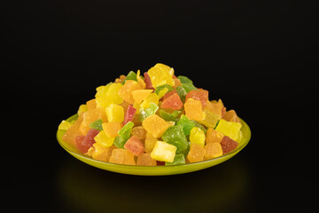 Colored mix sweets candied fruits in the saucer on black background. Fruit dessert yellow red pink...