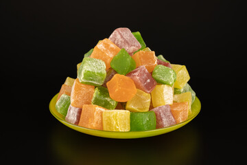 Colored mix sweets turkish delight in the saucer on black background. Fruit dessert yellow red pink green sprinkled with powdered sugar. Cooking concept delicious sweet food.