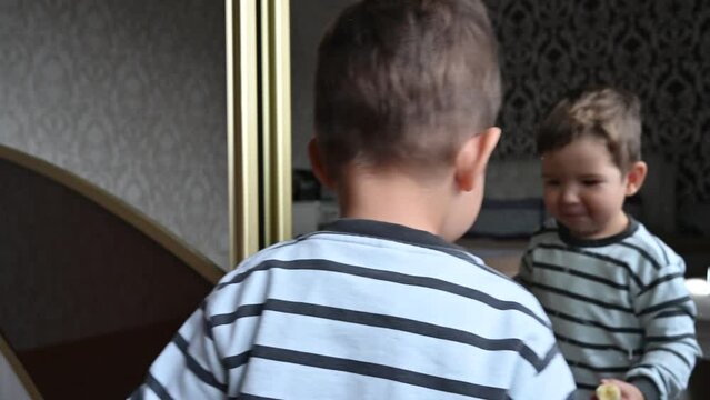 Toddler boy holding a slice of banana and dancing merrily in front of mirror