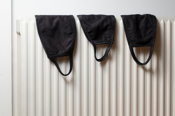Three black masks drying on white radiator