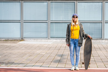 Fototapeta premium young happy and smiling girl with long board posing on a cycle, generation z fashionable woman living the city, minimal concept with copy space, yellow and blue palette