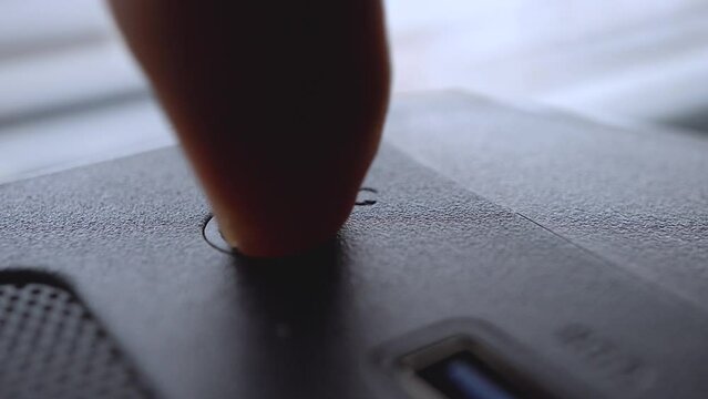 Macro video of a person turning on and off a personal computer with his finger. Turning on a device with a shallow depth of field.