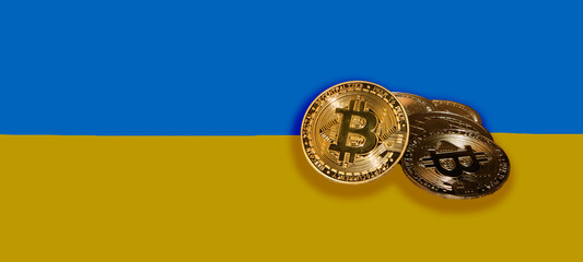 Panorama of several gold bitcoins and in the background a flag of Ukraine. Ukraine a country in need of crypto money.