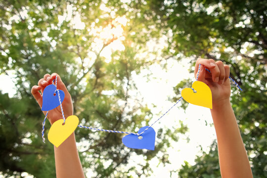 Image of hands holding blue and yellow paper hearts on a string, in support of Ukraine