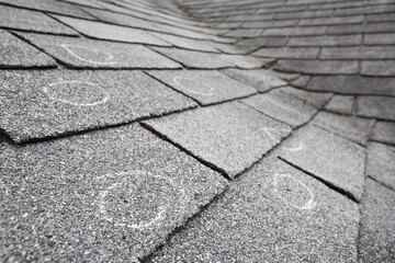 Old roof with hail damaged shingles, chalk circles mark the damage. Shallow depth of field