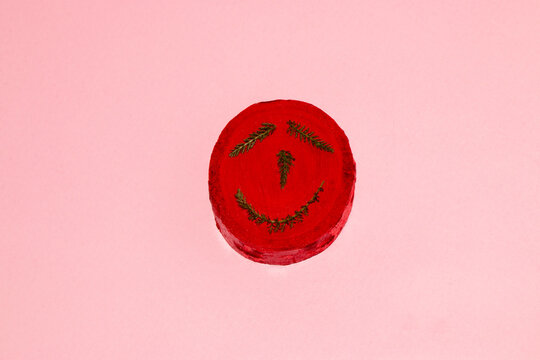 circle of wood painted red with grass creatively looks like a human head with facial expressions on a pink background