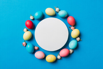 round frame multicolored Easter eggs with white blank paper on a brown background, close-up, space for text, blank for design, selective focus, tinted image