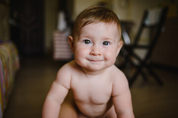 Portrait of a naked child. The baby stands and looks at the camera. Smiling, laughing, Indulging
