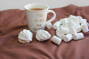 A cup of tea and an airy white marshmallow in a yellow plate on a pink background on a chocolate background