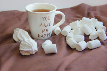 A cup of tea and an airy white marshmallow in a yellow plate on a pink background on a chocolate background