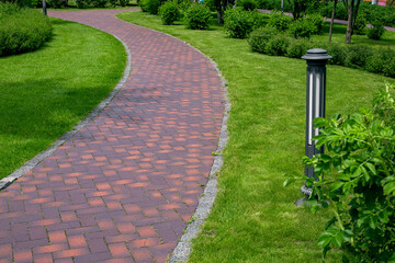 iron ground lantern garden lighting with curved path paved stone tiles in park among plants,...