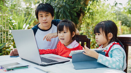 Family portrait of father and preschool daughters use computer for study at home. Dad teach his children to do coding homework via online classroom. Concept for work at home during covid-19 quarantine