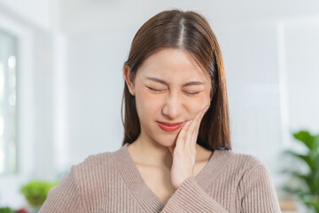Closing eyes asian young woman touching cheek, face expression from toothache, tooth decay or...