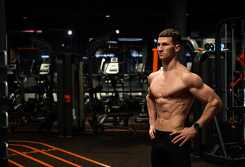 Athletic man with muscular fit torso standing with arms akimbo in gym, sportsman