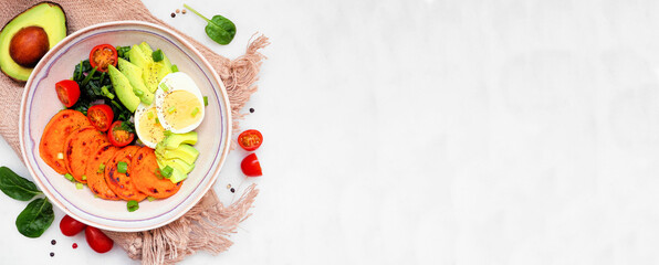 Nutritious breakfast bowl with sweet potato, egg, avocado and spinach. Overhead view table scene on a white marble banner background. Copy space.