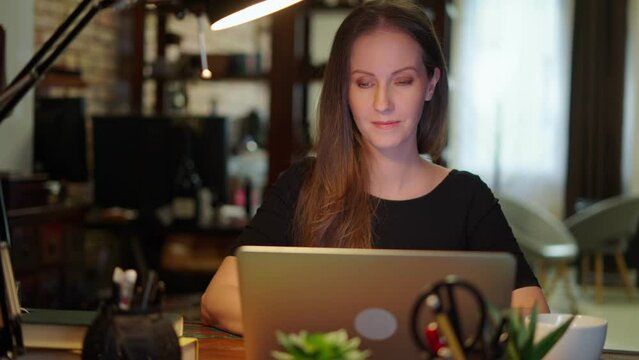 Businesswoman using laptop computer managing small business online in home office. Happy, smiling woman. Confident female entrepreneur.