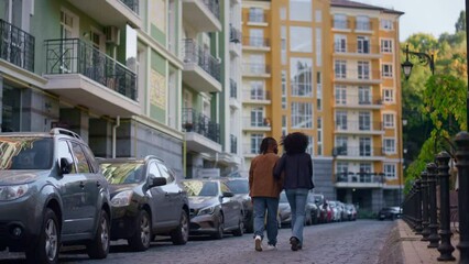 Married couple walking together at modern city residential complex rear view.